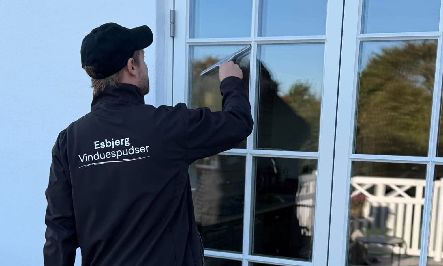 Vinduespudser trækker skraberen hen over ruden – traditionel håndpudsning