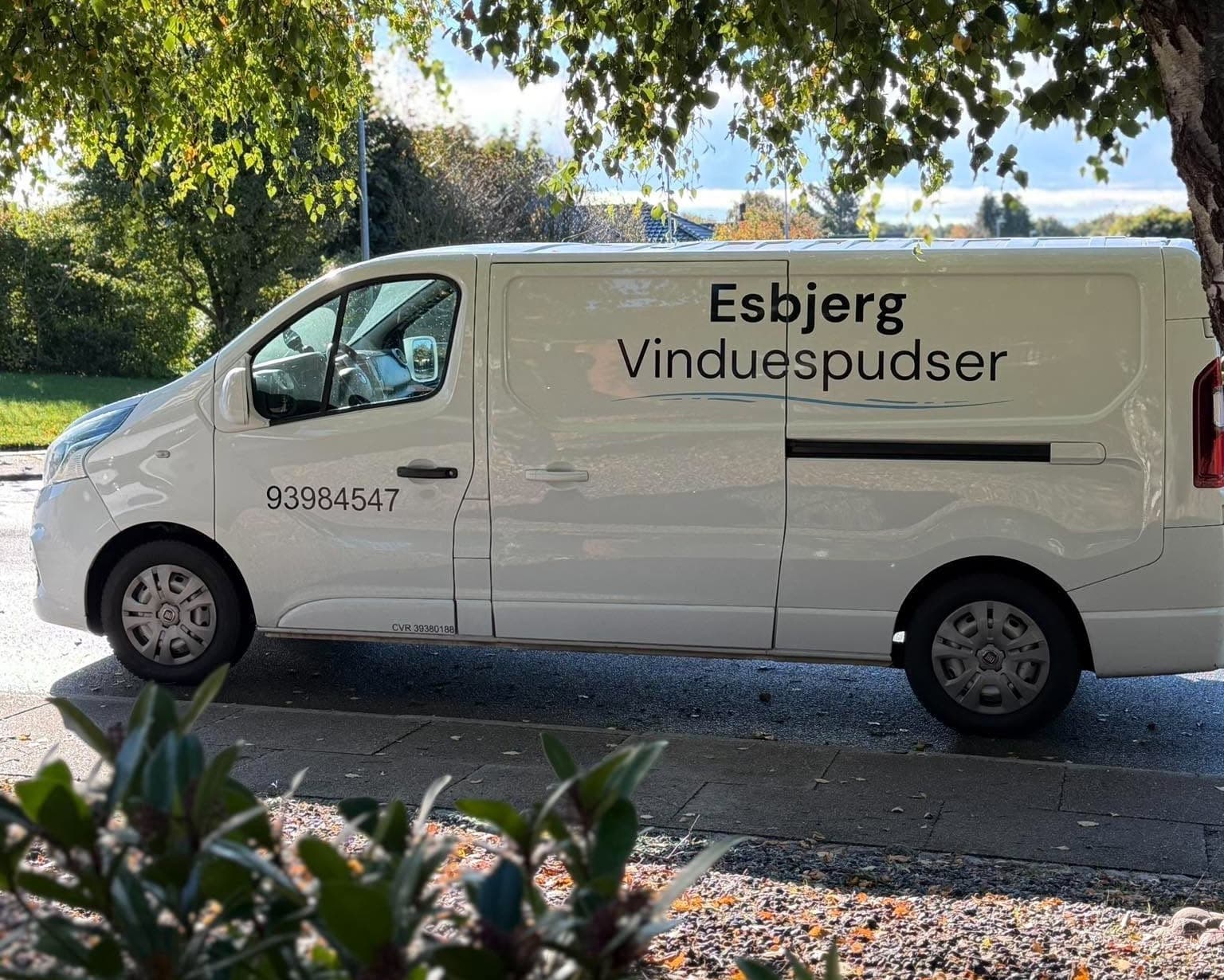 Hvid firmabil med Esbjerg Vinduespudser og telefonnummer på siden, parkeret under et træ